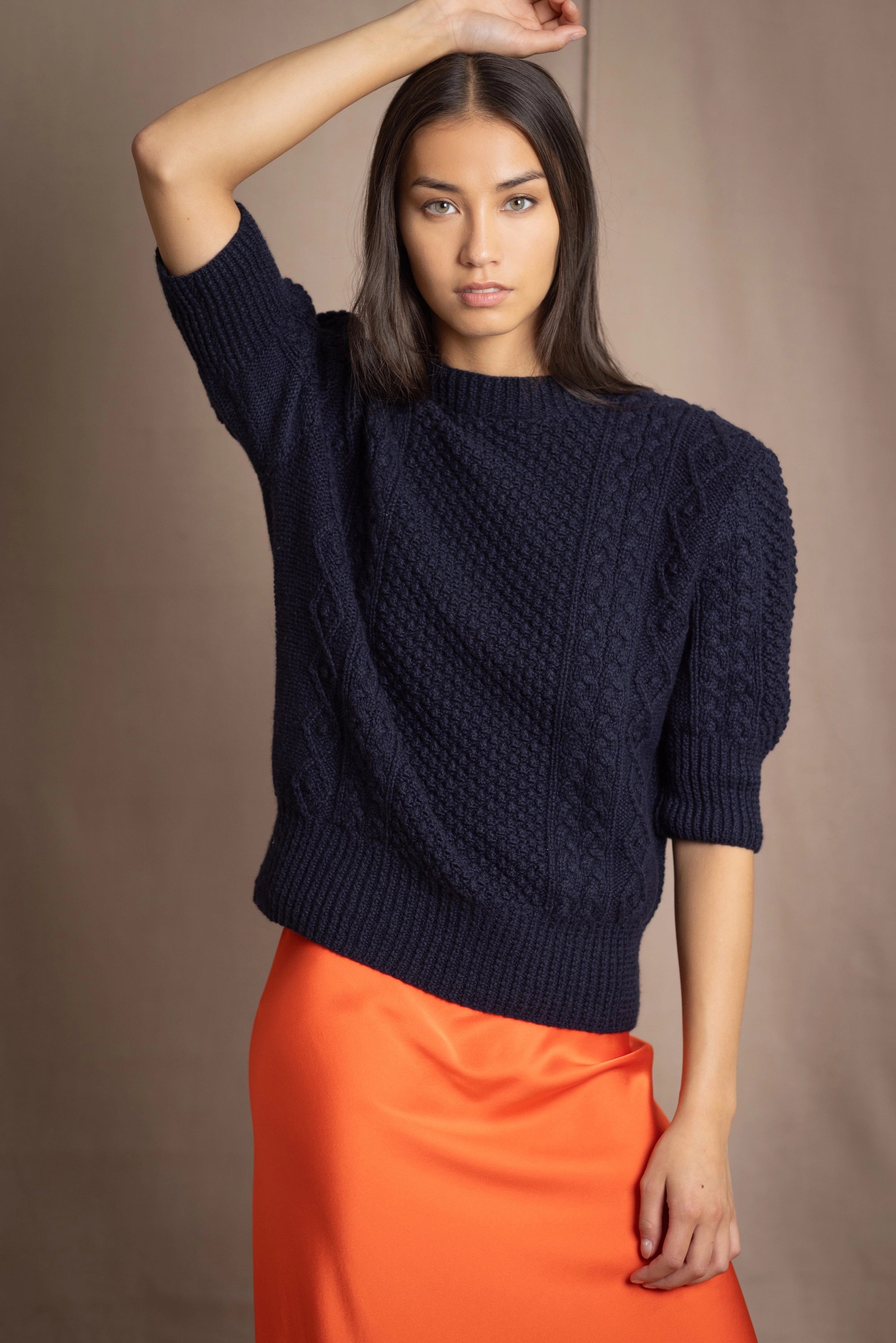a woman wearing a cashmere aran sweater tee in navy blue with orange silk skirt