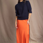 a woman wearing a cashmere aran sweater tee in navy blue with orange silk skirt