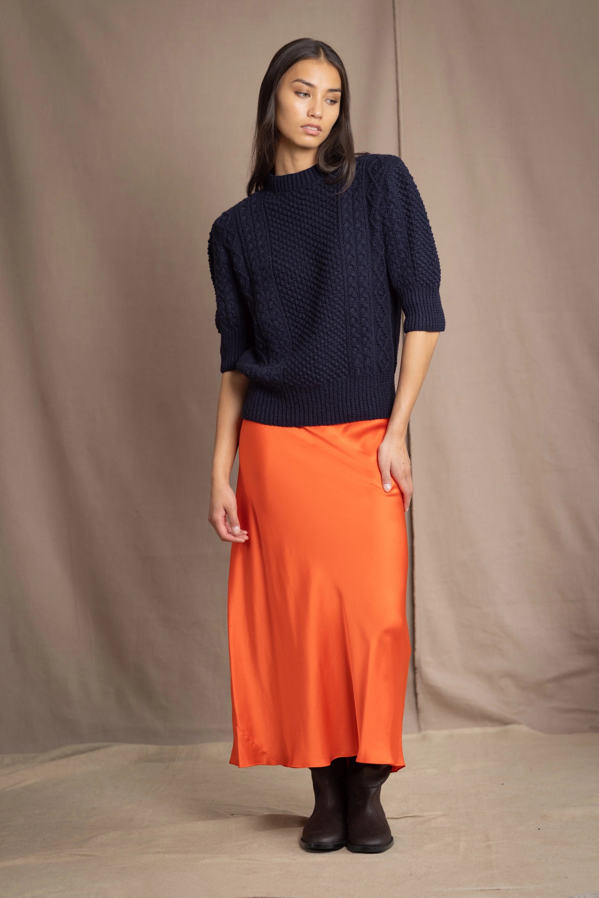a woman wearing a cashmere aran sweater tee in navy blue with orange silk skirt