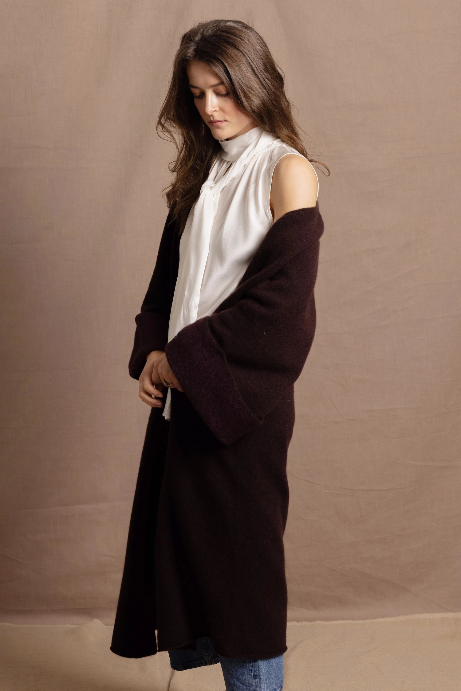 A woman wears a 100% silk pussybow sleeveless blouse in white with a chocolate brown and purple cashmere coat on top