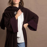 A woman wears a 100% silk pussybow sleeveless blouse in white with a chocolate brown and purple cashmere coat on top with matching wrap
