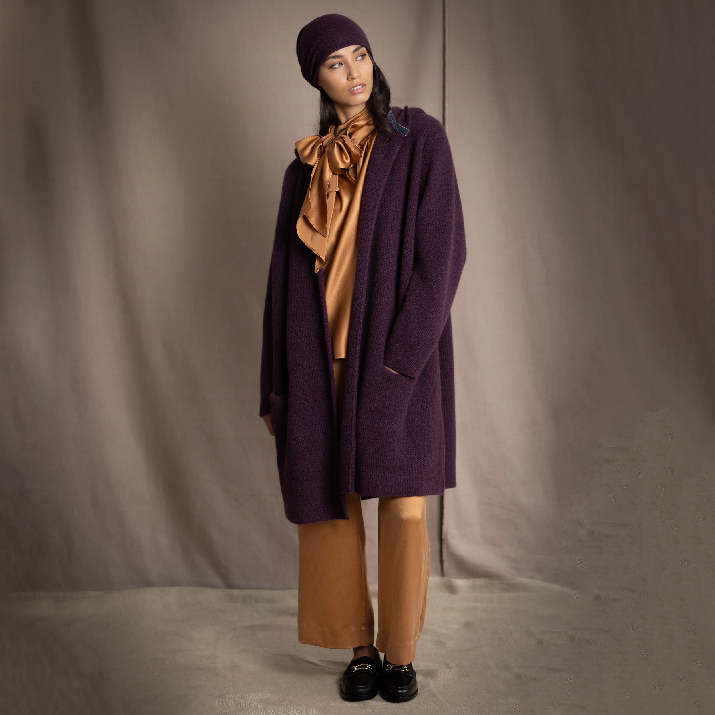 Woman wearing a cashmere coat and hat in purple with a silk top and silk trousers in gold