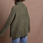 a lady wears a 100% cashmere aran sweater in fern green