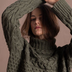 a lady wears a 100% cashmere aran sweater in fern green