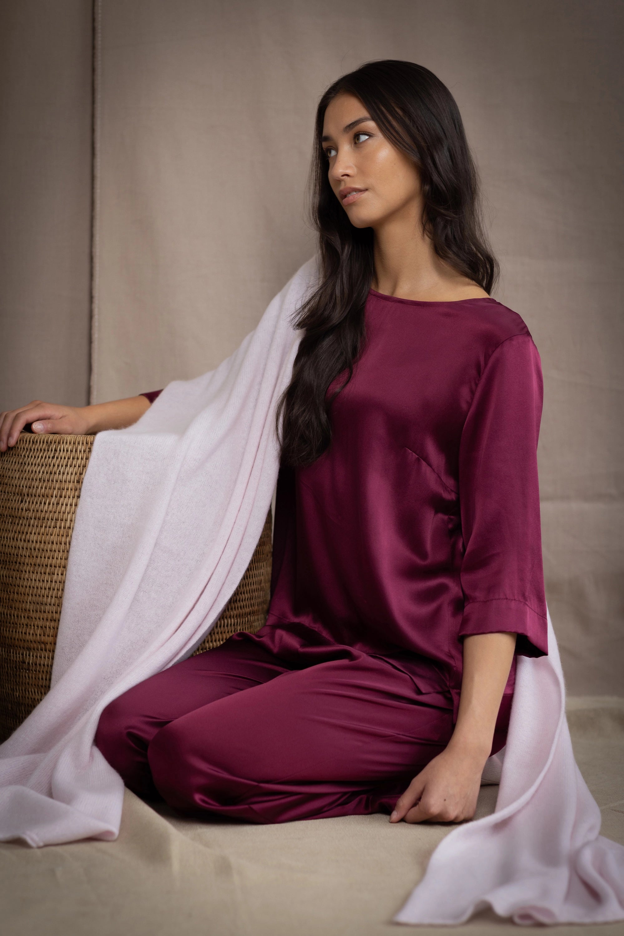 a woman wearing a large cashmere wrap shawl in pale pink over burgundy silk top and trousers