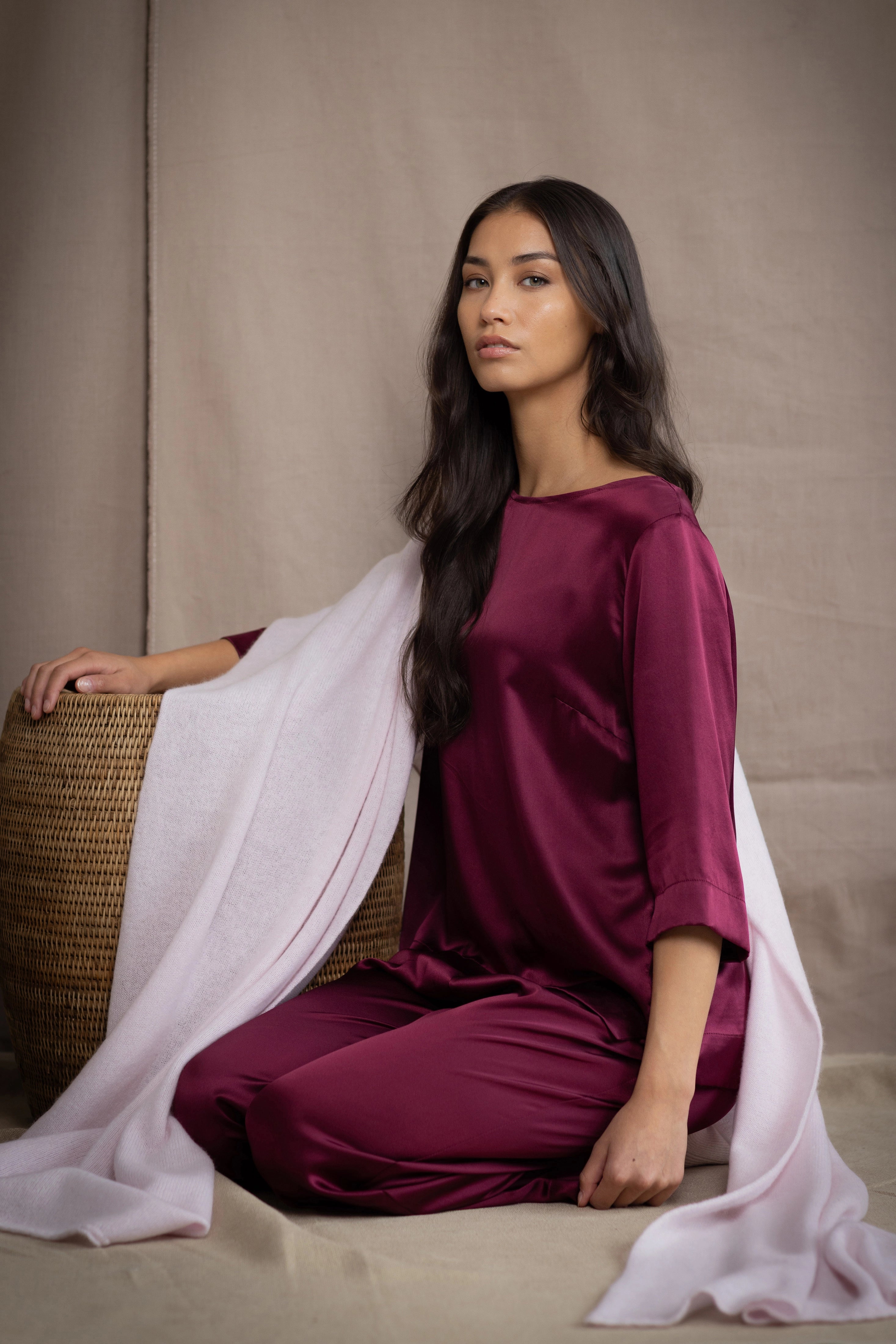 a woman wearing a large cashmere wrap shawl in pale pink over burgundy silk top and trousers