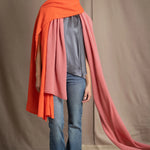 a woman wears a large cashmere wrap shawl in bright orange layered over another cashmere wrap in dusty rose pink