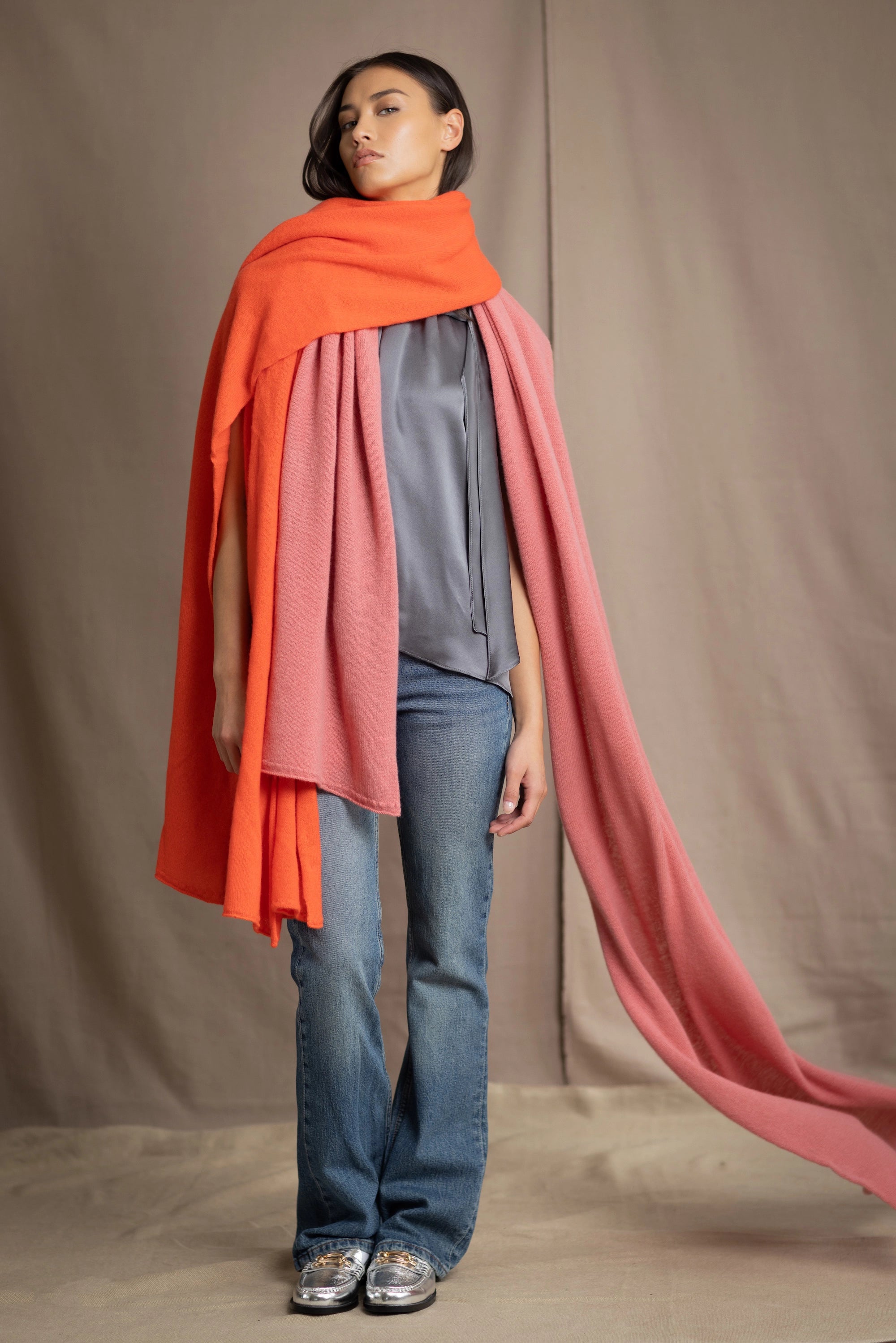 a woman wears a large cashmere wrap shawl in bright orange layered over another cashmere wrap in dusty rose pink