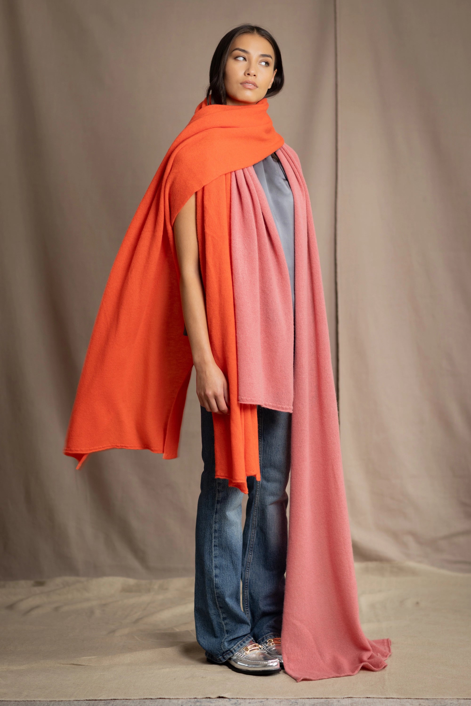 a woman wears a large cashmere wrap shawl in bright orange layered with a cashmere wrap in dusty rose pink