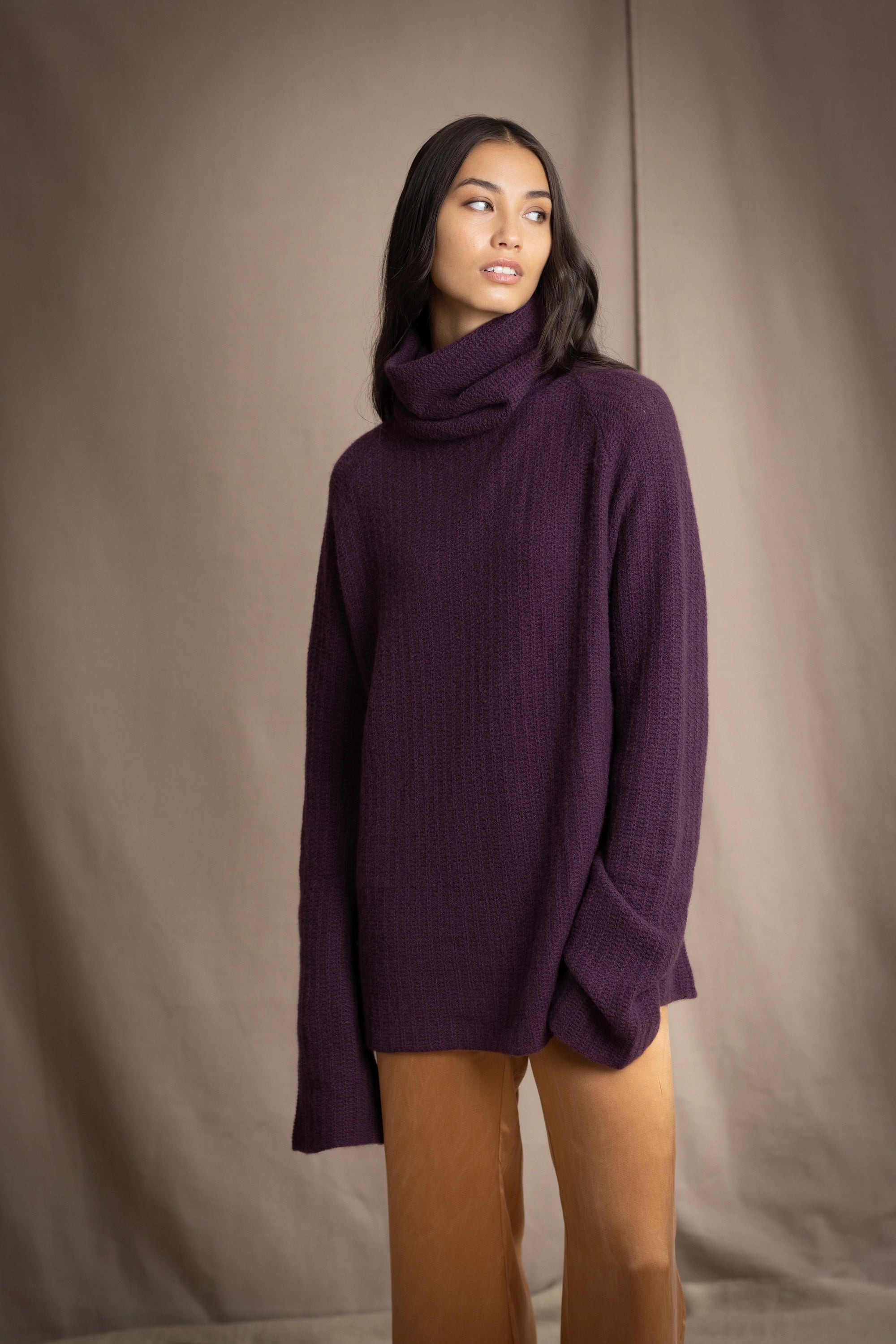 Woman wearing a cashmere fisherman turtleneck sweater in dark purple with bronze silk trousers