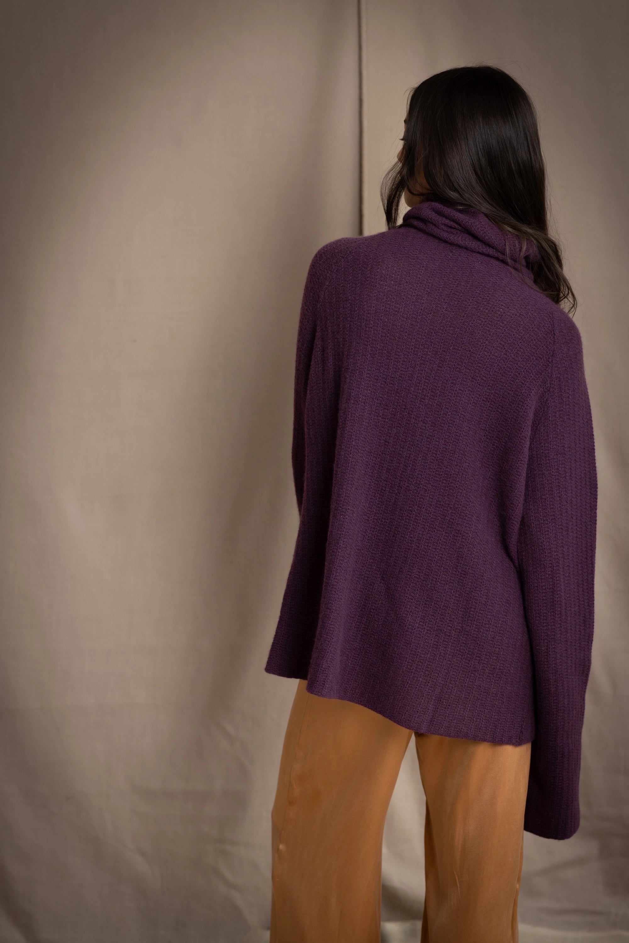 Woman wearing a cashmere fisherman turtleneck sweater in dark purple with bronze silk trousers