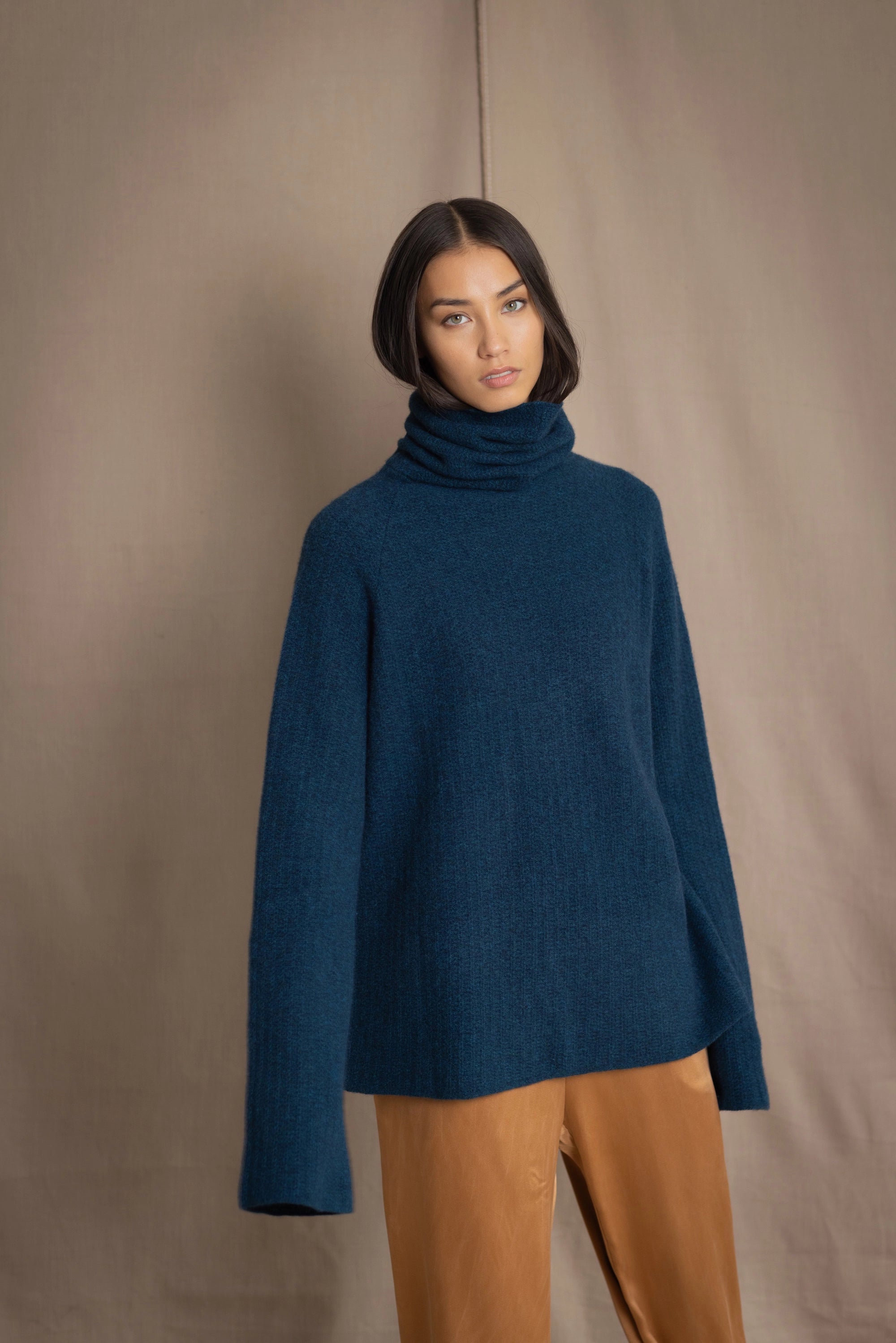 Woman wearing a cashmere fisherman turtleneck sweater in teal blue with bronze silk trousers
