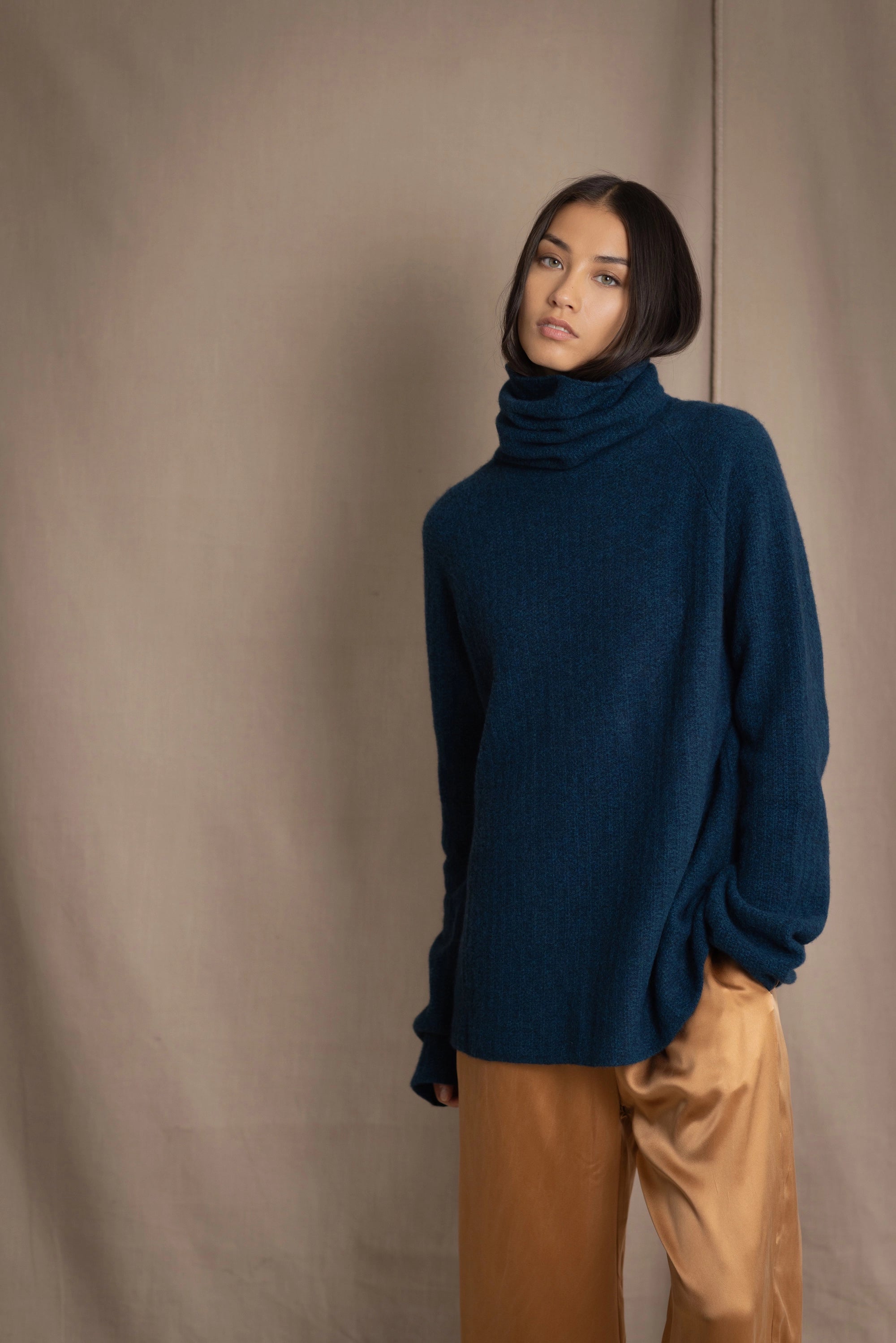 Woman wearing a cashmere fisherman turtleneck sweater in teal blue with bronze silk trousers