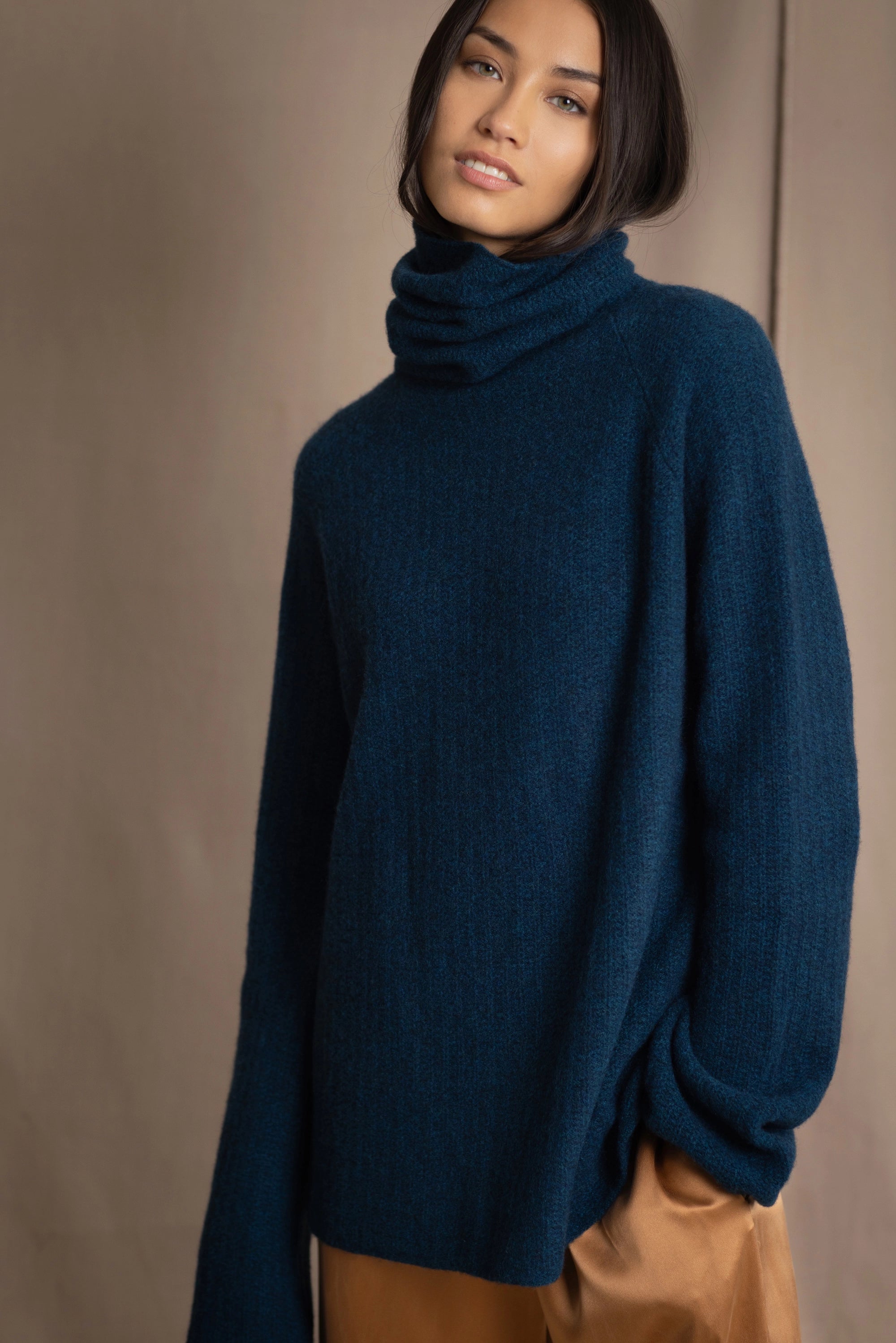 Woman wearing a cashmere fisherman turtleneck sweater in teal blue with bronze silk trousers