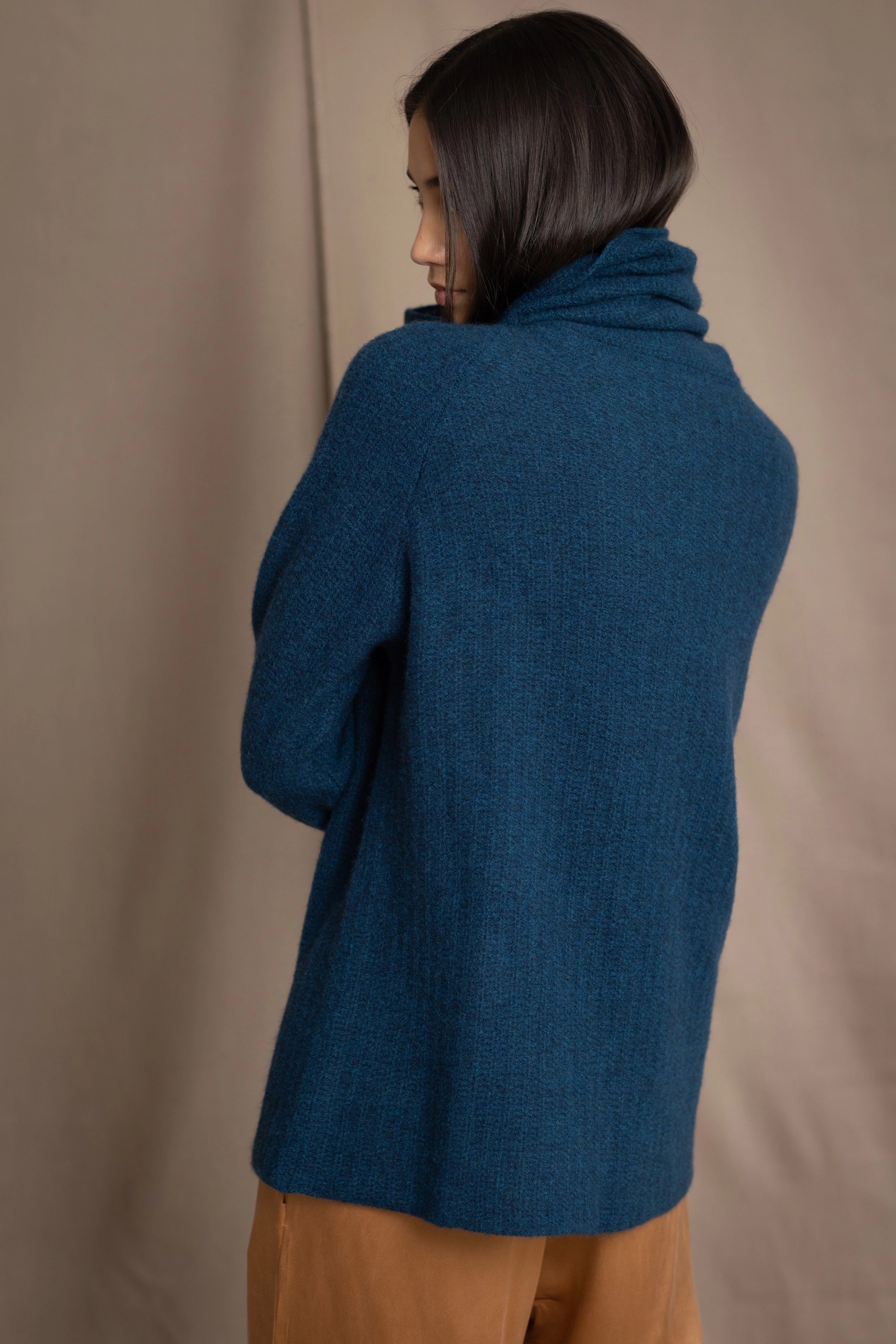 Woman wearing a cashmere fisherman turtleneck sweater in teal blue with bronze silk trousers