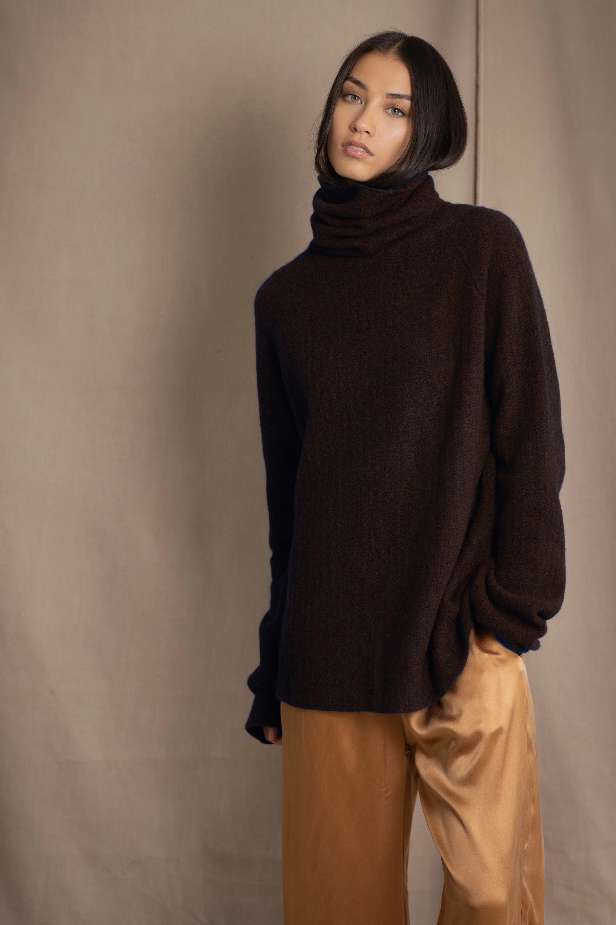 Woman wearing a dark brown fisherman knitted turtleneck sweater  jumper and bronze silk pants