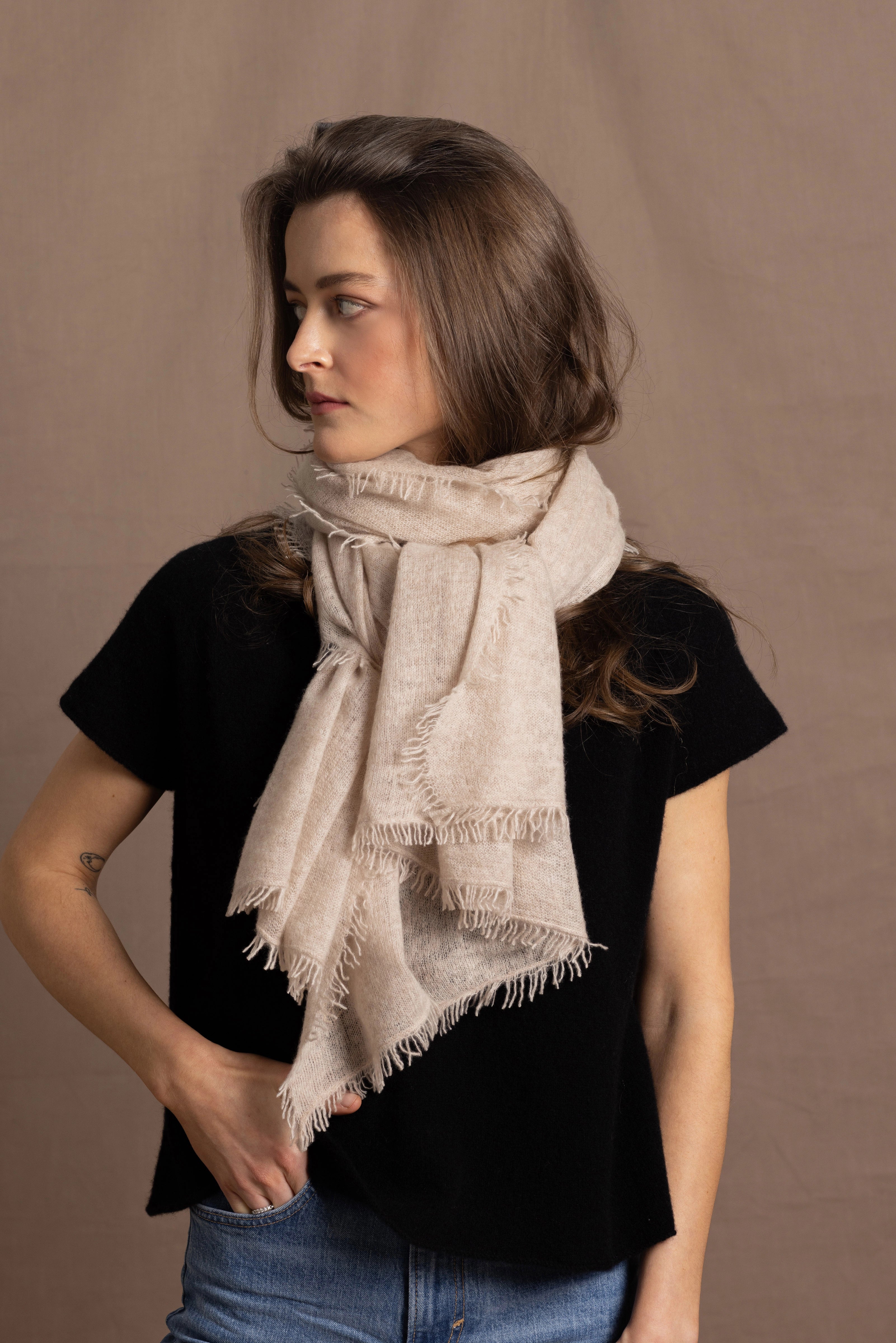 A woman wears a lightweight, fine cashmere wrap scarf tied around her neck with a black cashmere t-shirt underneath