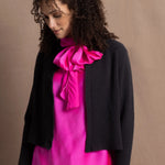 A woman wears a 100% cashmere cropped cardigan on top in navy blue over a 100% pure silk top in bright shocking pink over matching trousers