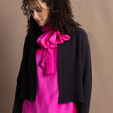 A woman wears a 100% cashmere cropped cardigan on top in navy blue over a 100% pure silk top in bright shocking pink over matching trousers