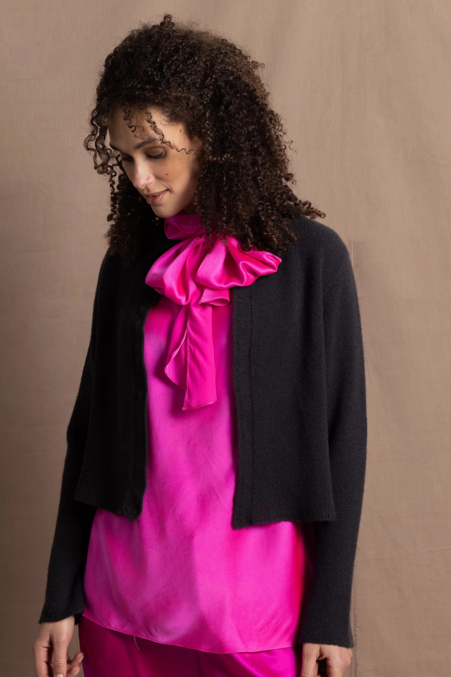 A woman wears a 100% cashmere cropped cardigan on top in navy blue over a 100% pure silk top in bright shocking pink over matching trousers