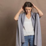 A woman wears a 100% cashmere wrap shawl in grey over a silk top in white