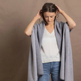 A woman wears a 100% cashmere wrap shawl in grey over a silk top in white