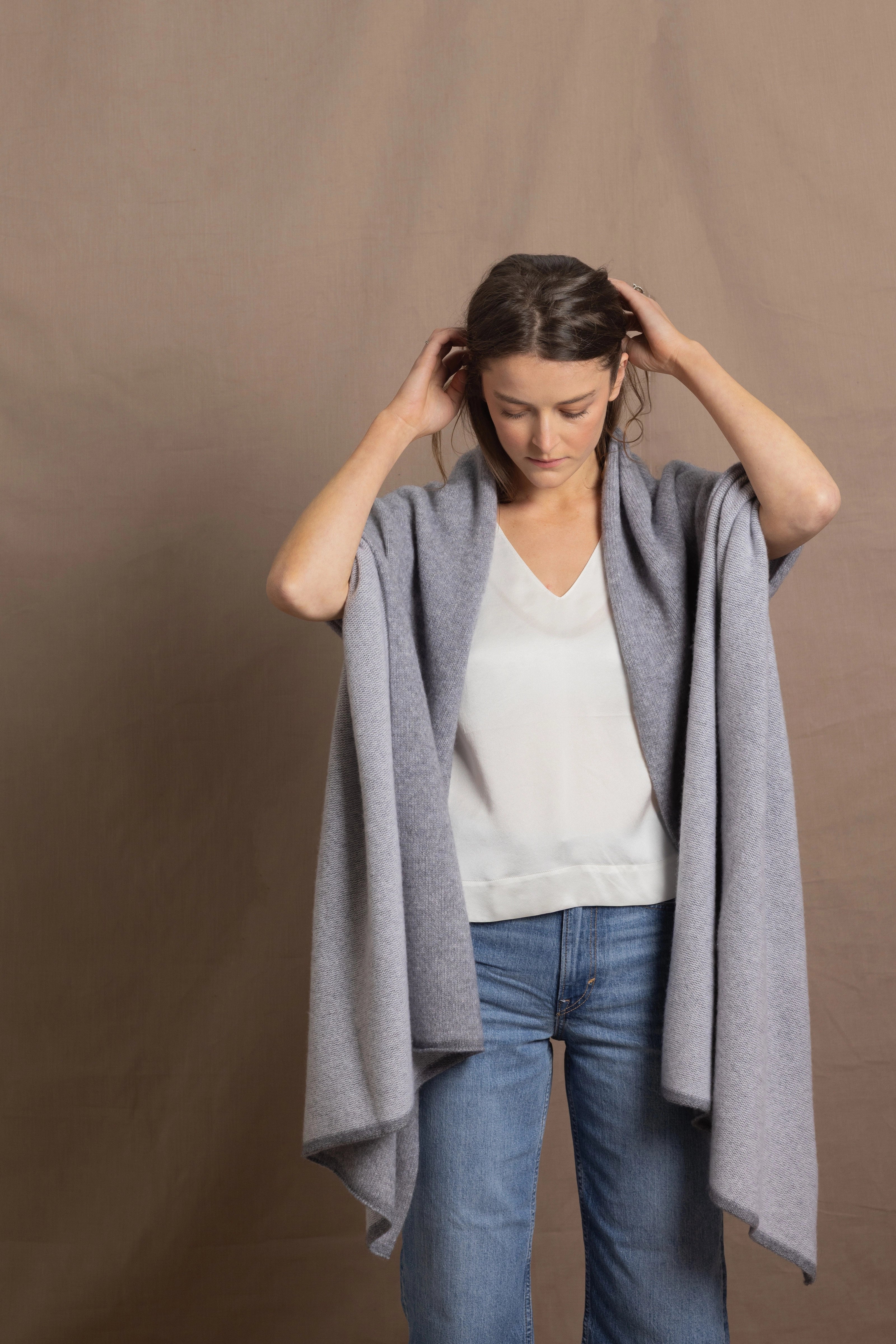 A woman wears a 100% cashmere wrap shawl in grey over a silk top in white