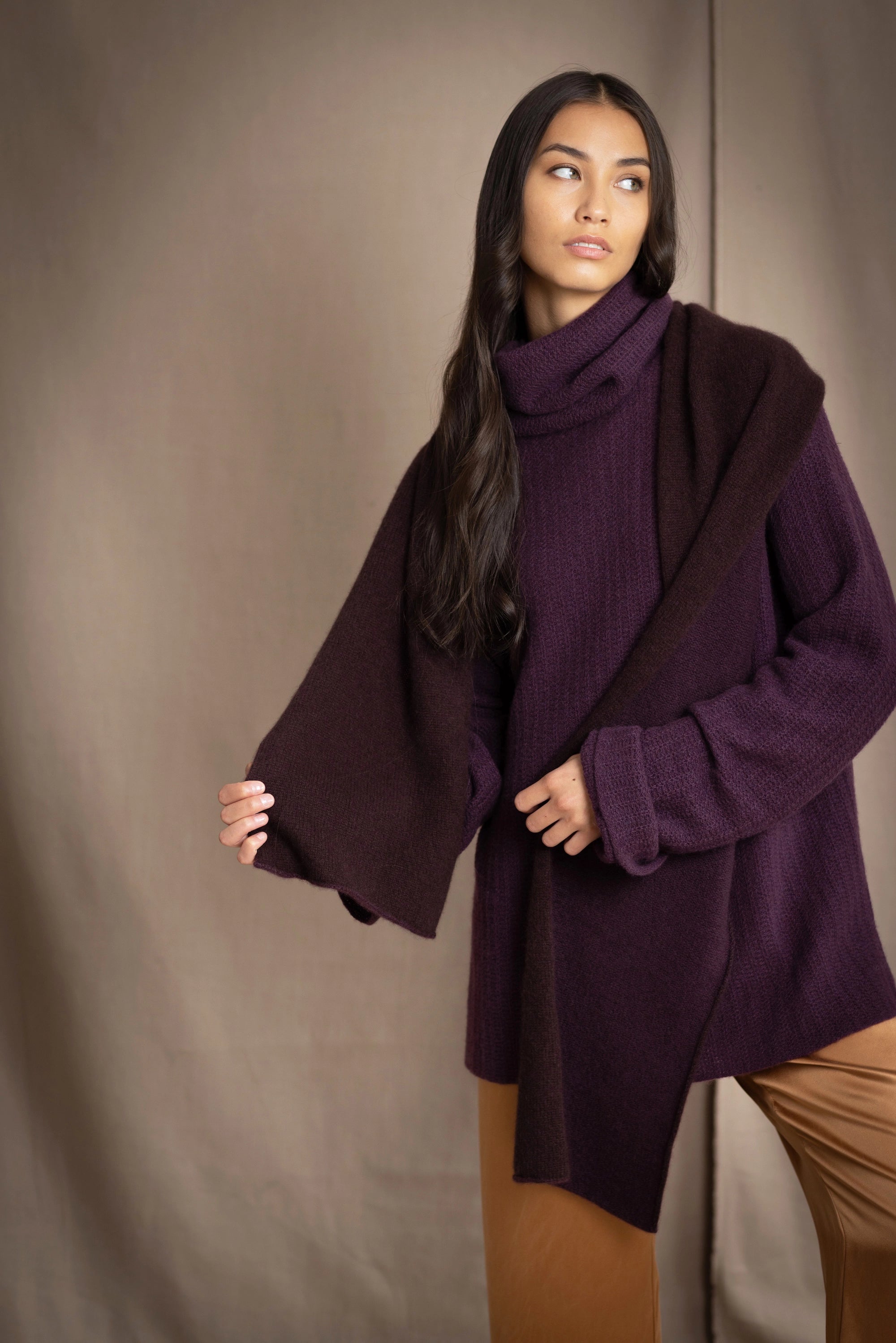 Woman wearing a cashmere fisherman turtleneck sweater in dark purple with bronze silk trousers and a brown and dark purple reversible cashmere scarf