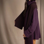 woman wears a reversible cashmere scarf in dark purple and dark brown on the other side worn over a dark purple cashmere sweater and bronze silk trousers