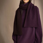 woman wears a reversible cashmere scarf in dark purple and dark brown on the other side worn over a dark purple cashmere sweater and bronze silk trousers