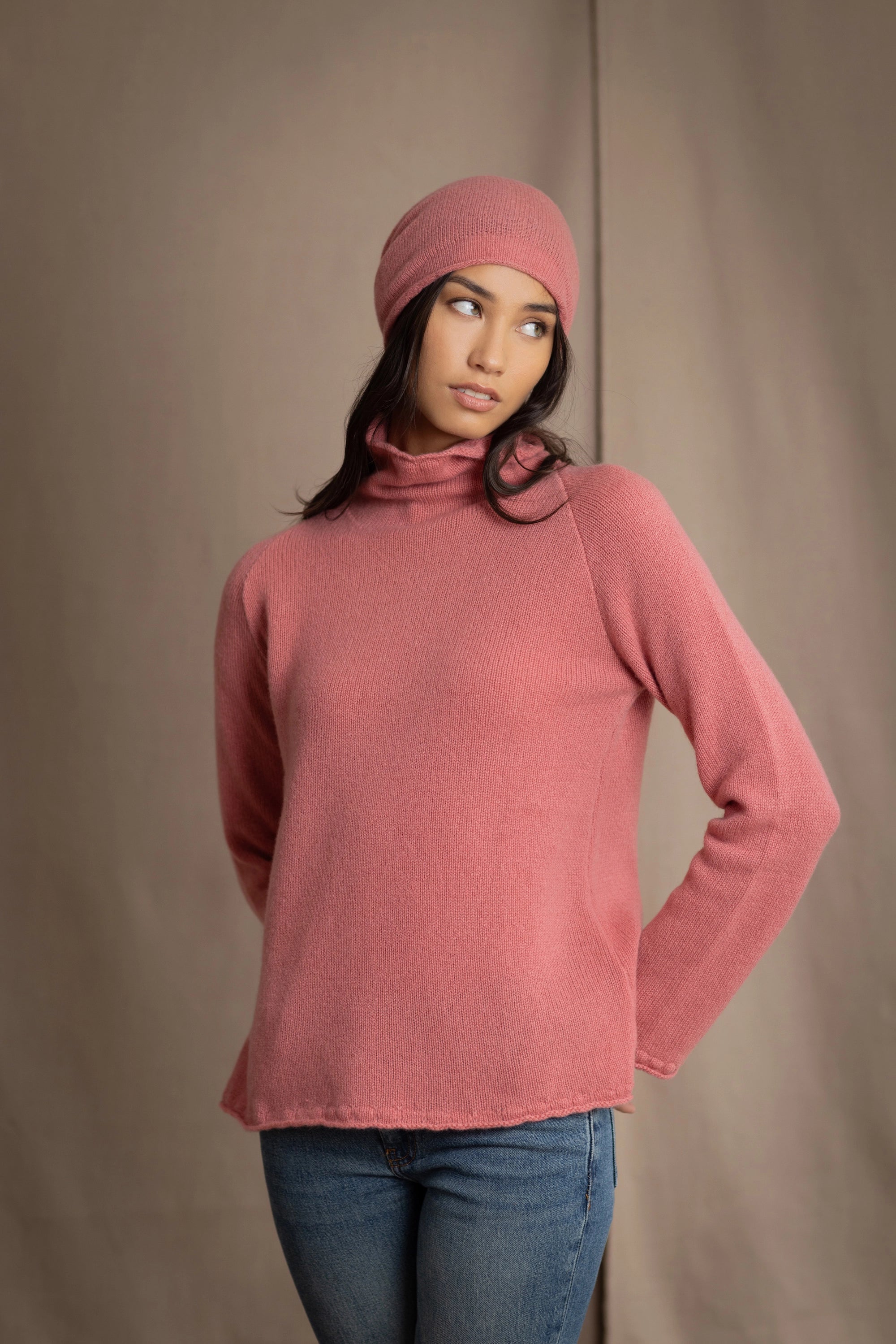 a woman wearing a cashmere turtleneck sweater in dusty rose pink and matching cashmere beanie hat in dusty rose pink