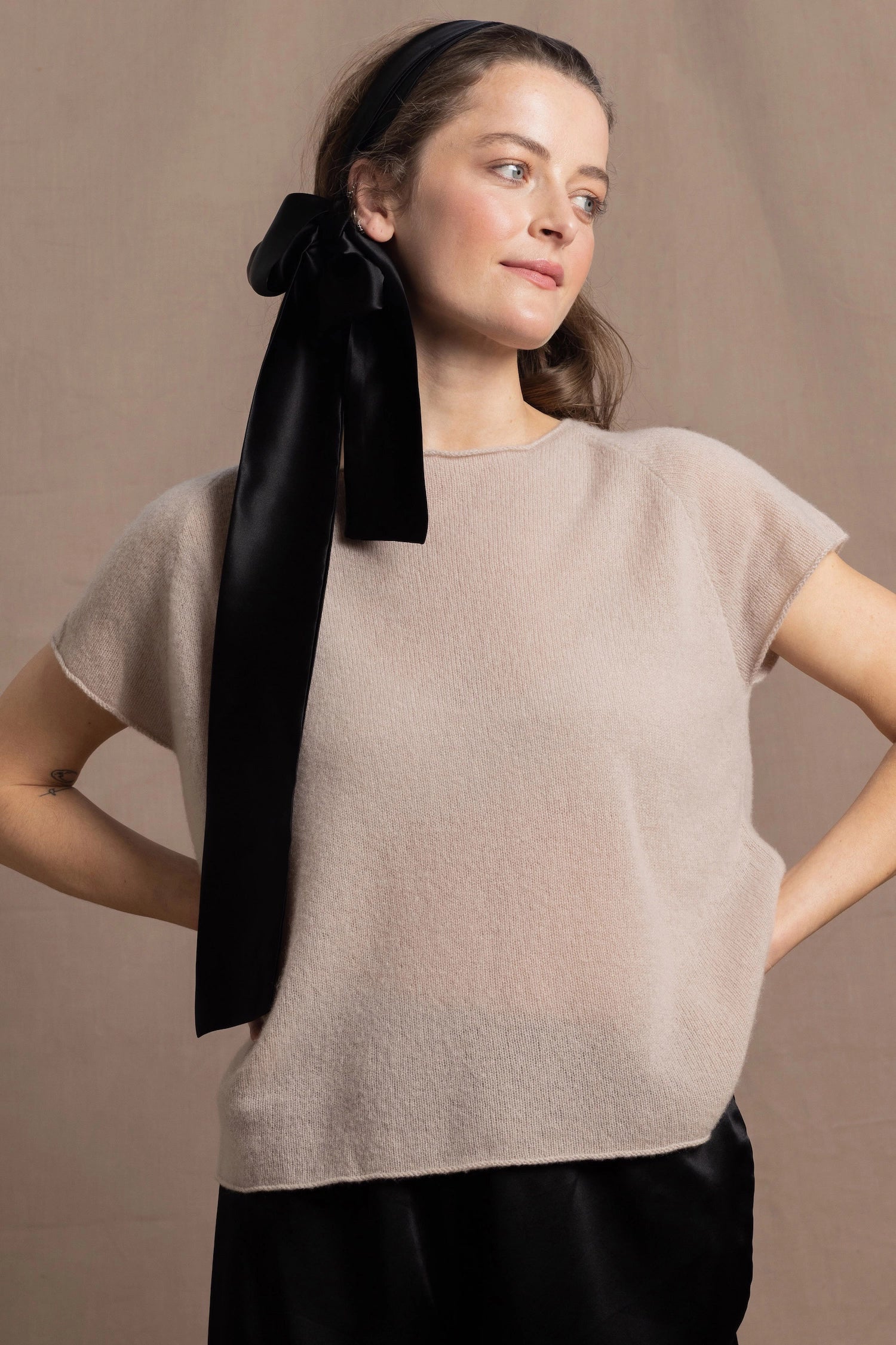 A woman wears a 100% cashmere tshirt in beige with a black silk tie in her hair and black silk shorts