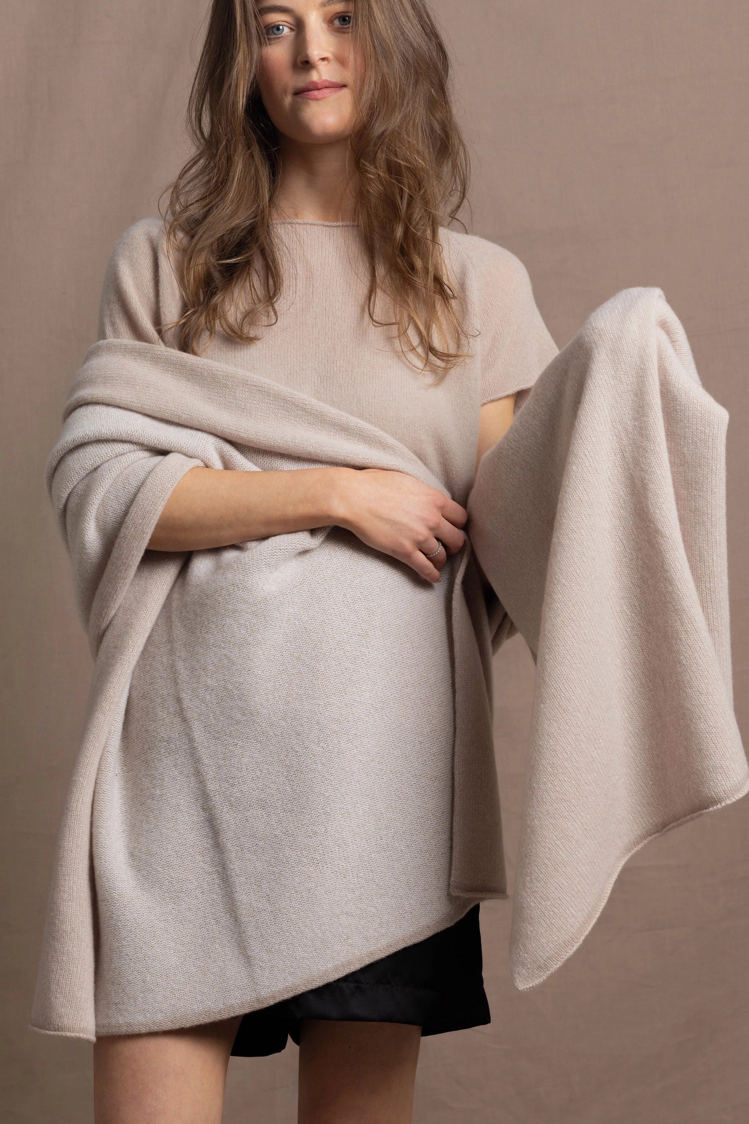 A woman wears a large cashmere shawl in beige over a matching cashmere tee