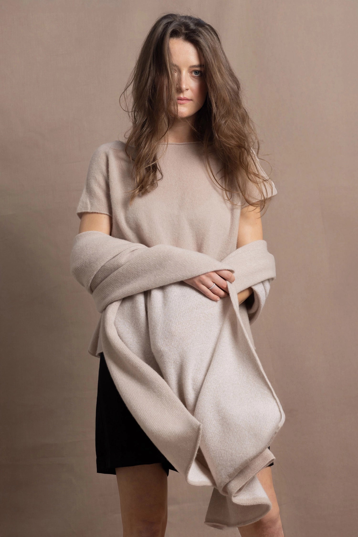 A woman wears a large cashmere shawl in beige over a matching cashmere tee