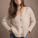 a woman wears a beige coloured cashmere aran cardigan sweater with horn buttons on it and diamond stitches