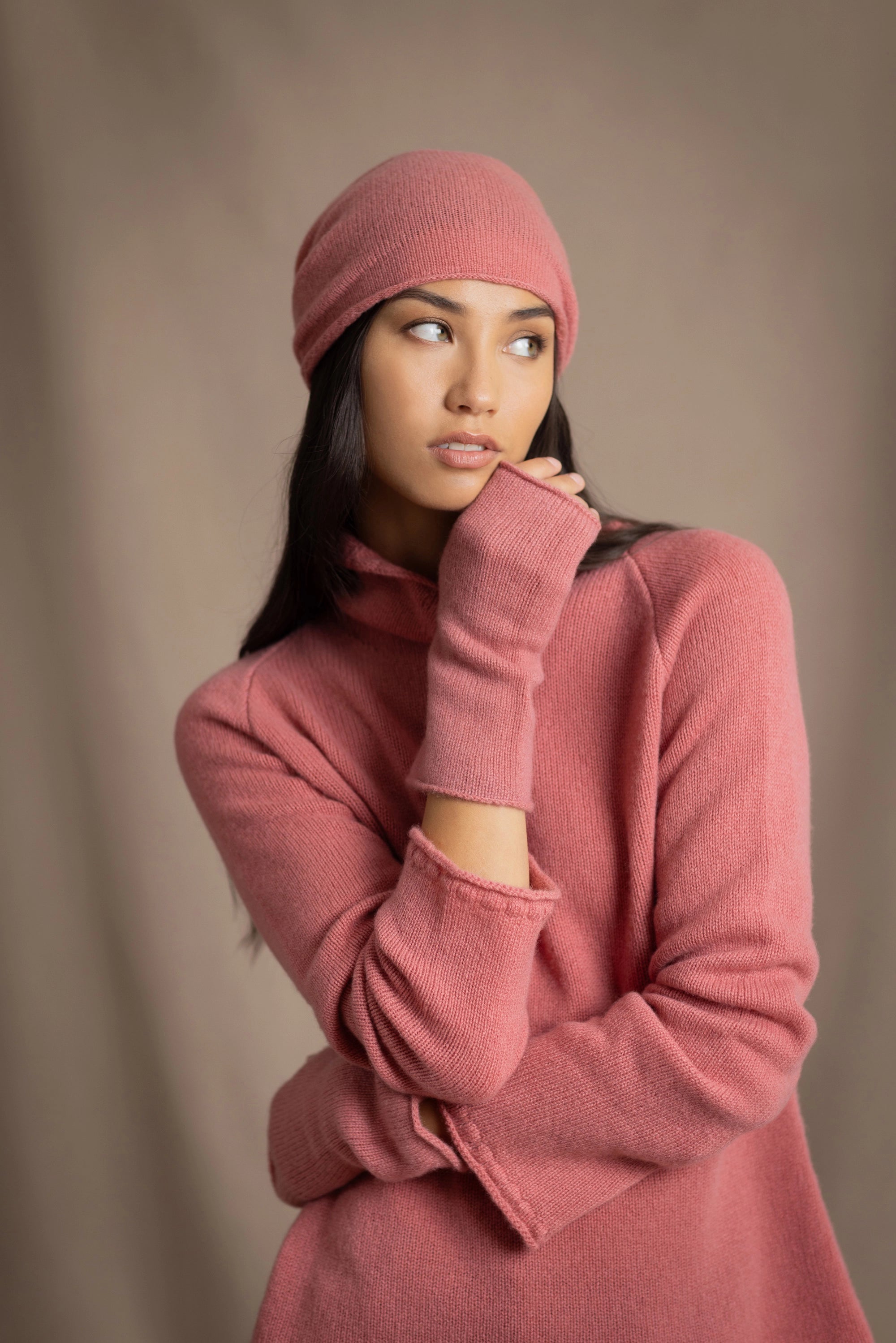 a woman wearing a cashmere turtleneck sweater in dusty rose pink and matching cashmere beanie hat and fingerless gloves in dusty rose pink