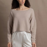 A woman wears a cropped cashmere sweater in beige with white silk shorts