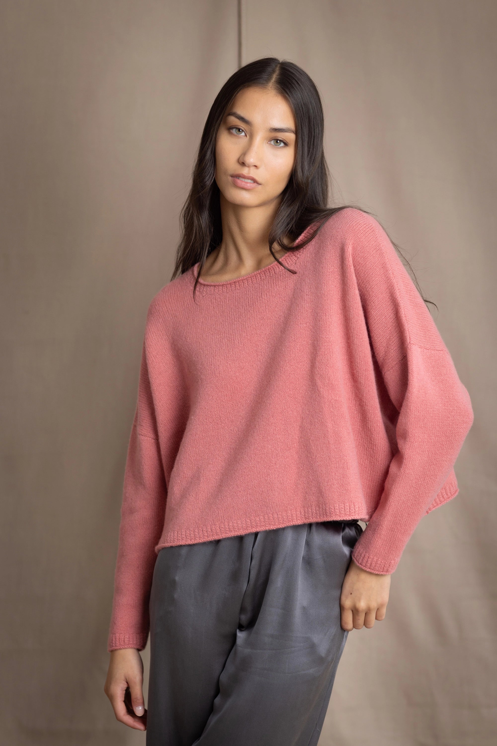 a woman wearing a cropped cashmere oversized cashmere sweater in dusty rose pink over silk trousers in pewter grey