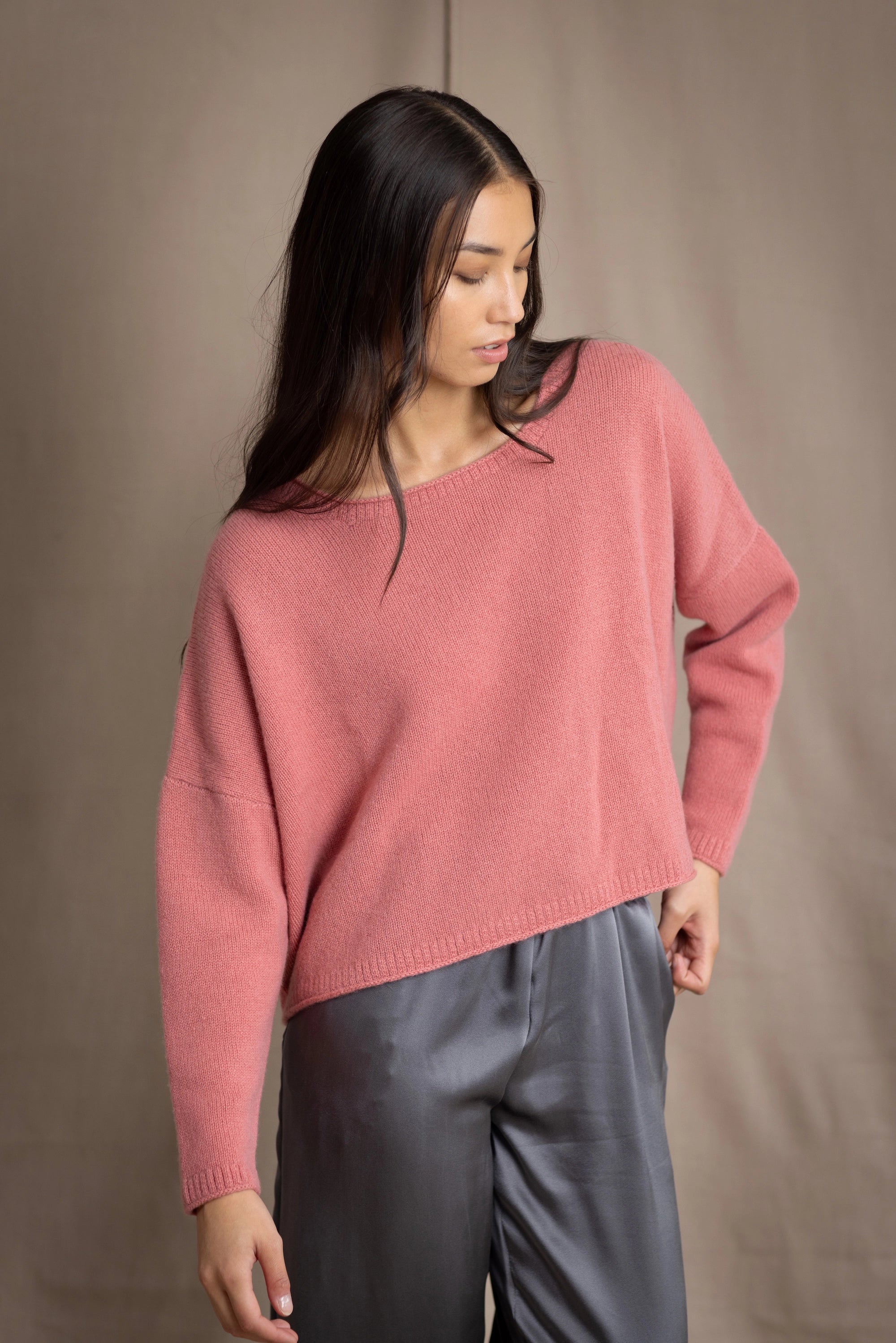 a woman wearing a cropped cashmere oversized cashmere sweater in dusty rose pink over silk trousers in pewter grey