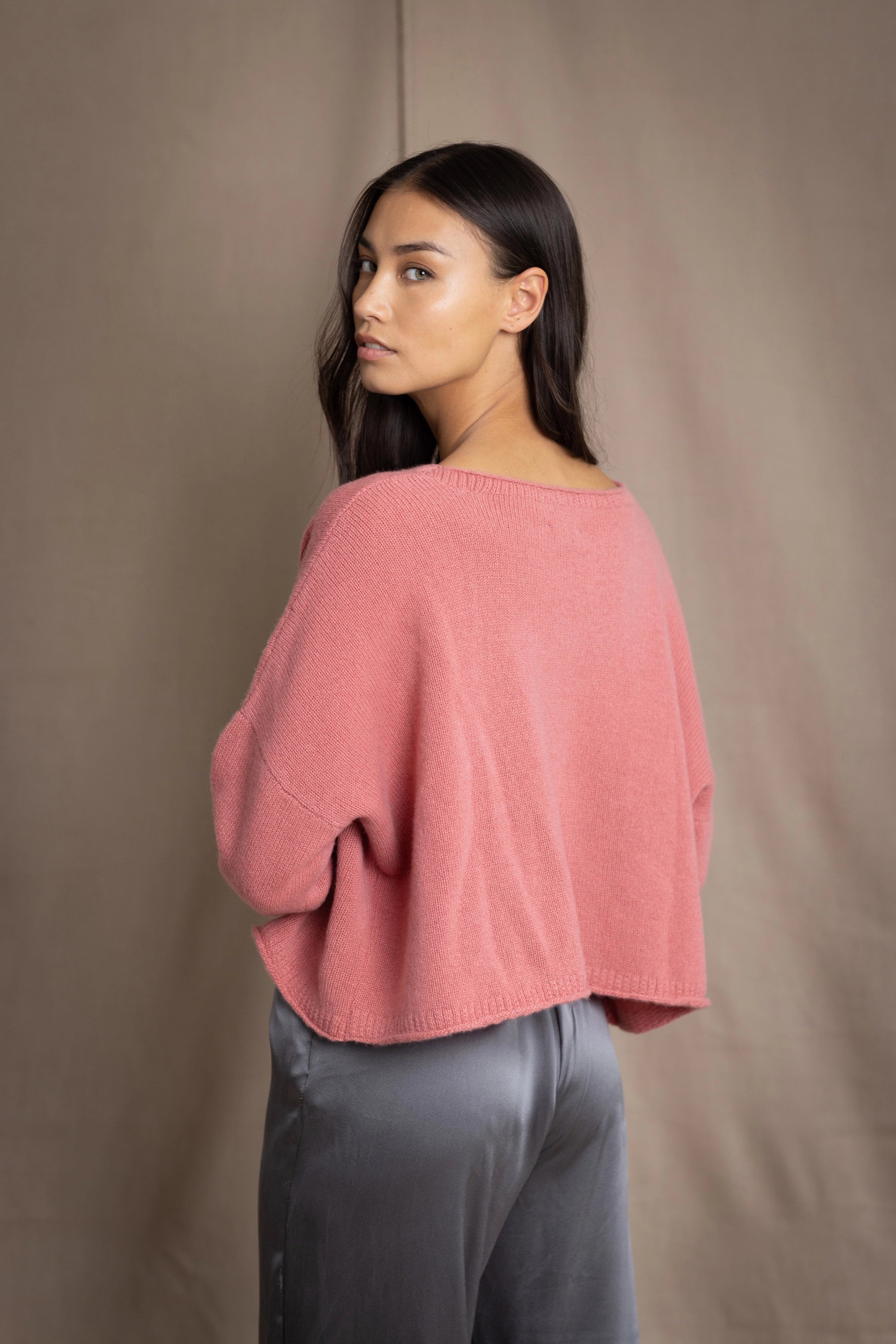 a woman wearing a cropped cashmere oversized cashmere sweater in dusty rose pink over silk trousers in pewter grey