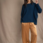 a woman wearing an oversized cashmere sweater in teal blue over silk trousers in bronze