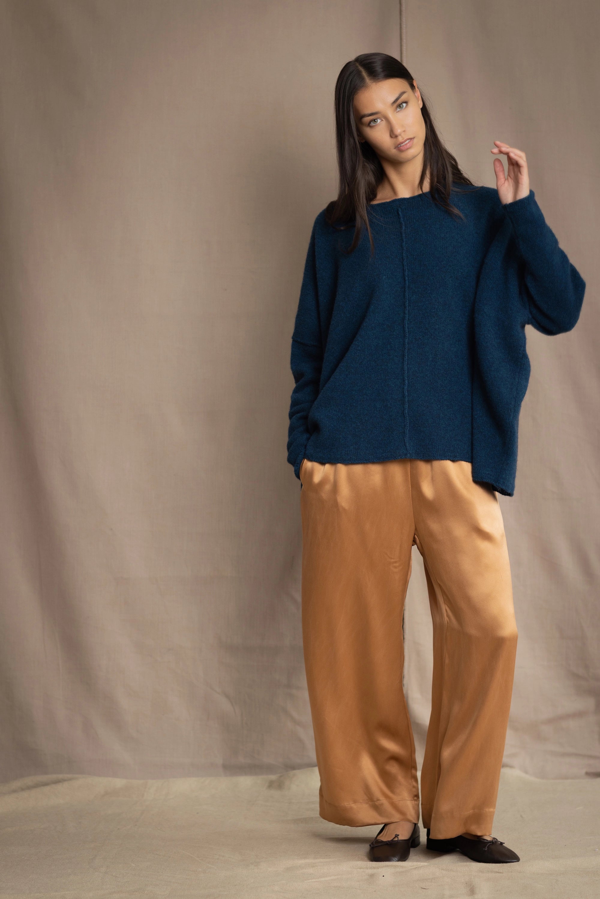 a woman wearing an oversized cashmere sweater in teal blue over silk trousers in bronze