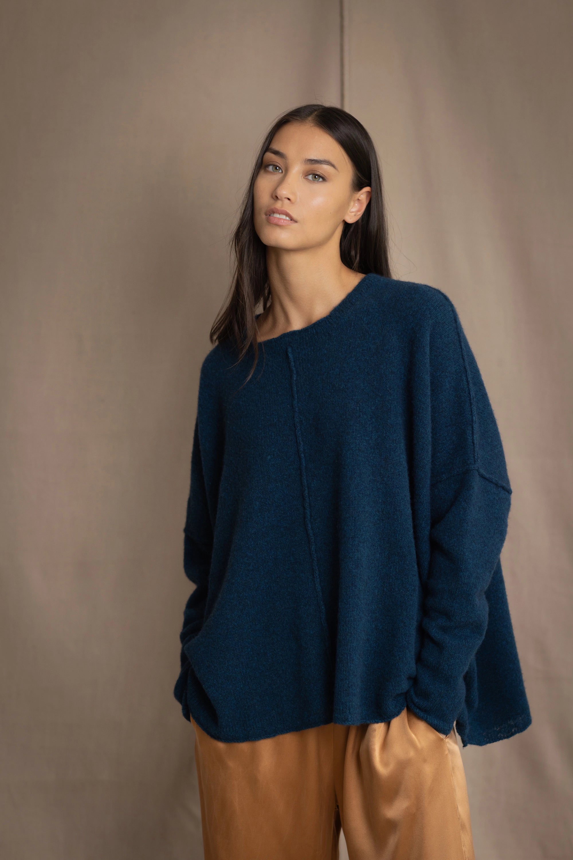 a woman wearing an oversized cashmere sweater in teal blue over silk trousers in bronze