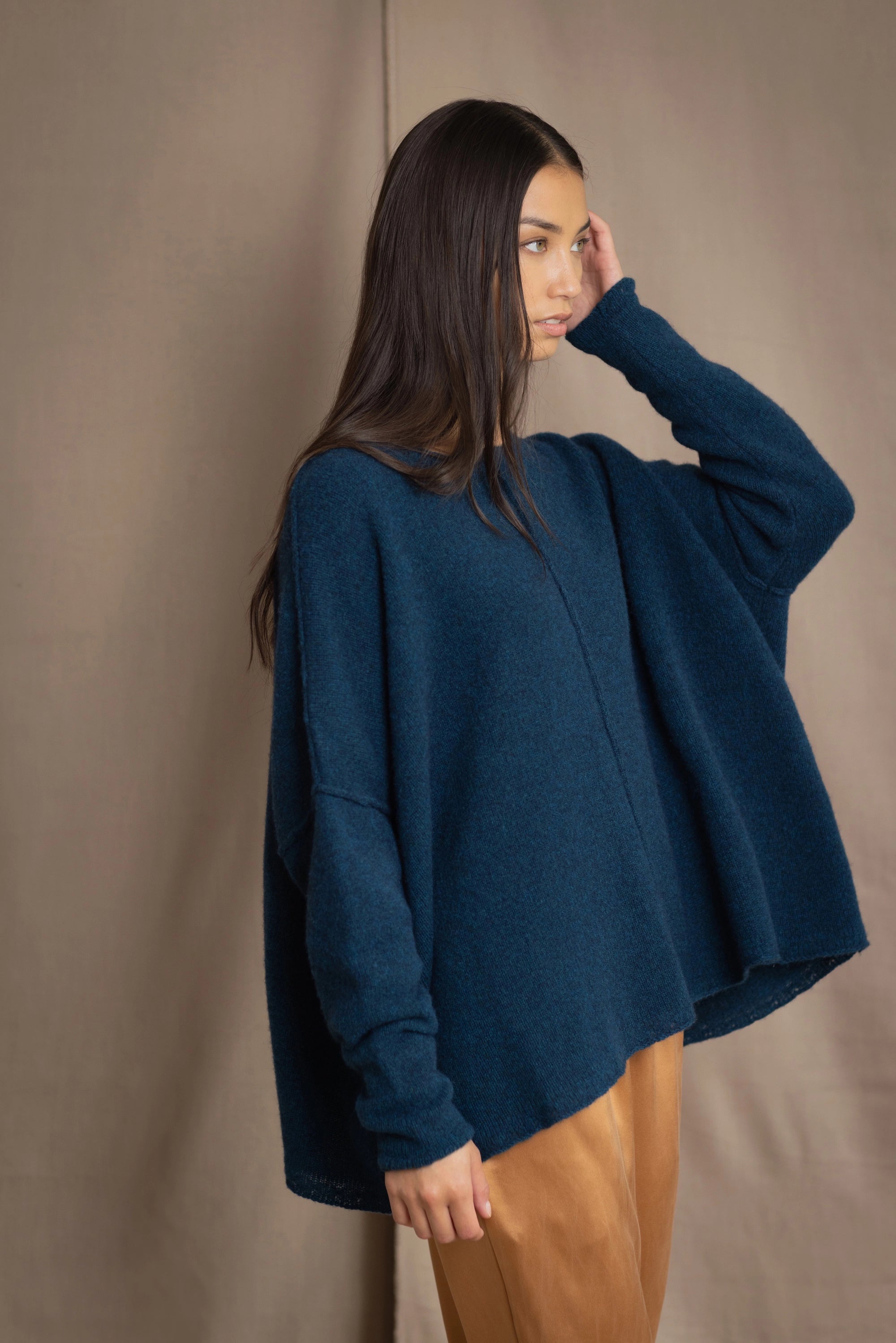 a woman wearing an oversized cashmere sweater in teal blue over silk trousers in bronze