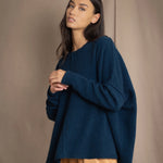 a woman wearing an oversized cashmere sweater in teal blue over silk trousers in bronze