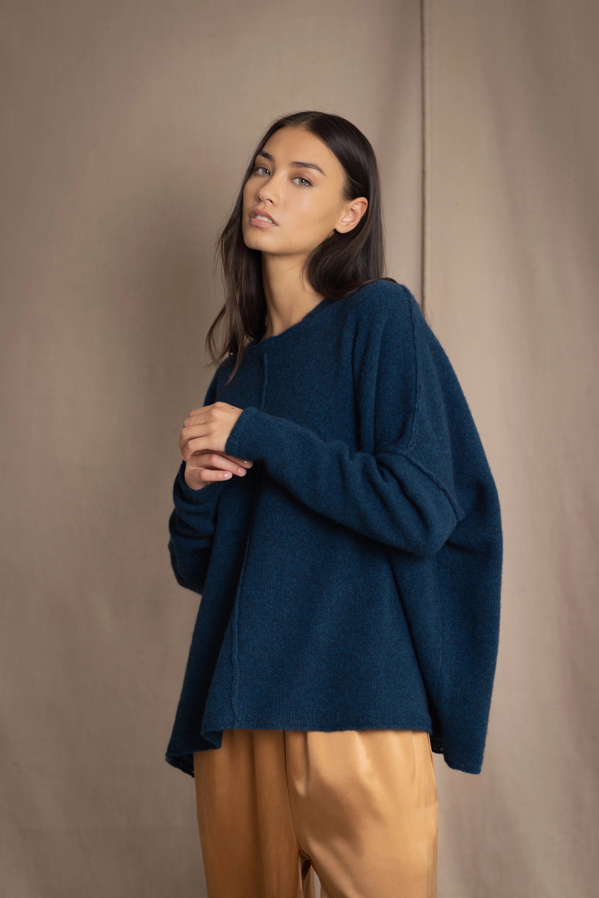 a woman wearing an oversized cashmere sweater in teal blue over silk trousers in bronze