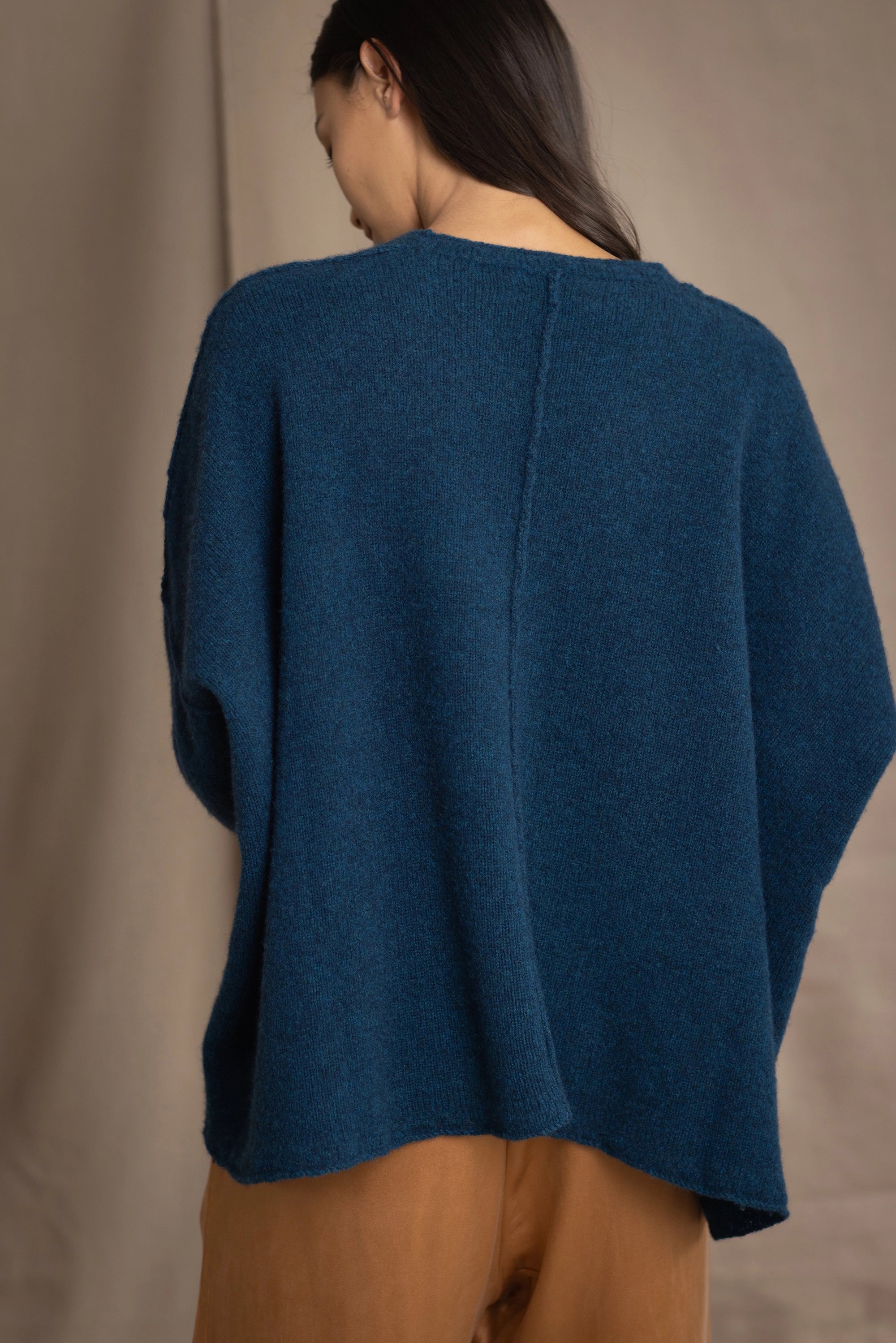 a woman wearing an oversized cashmere sweater in teal blue over silk trousers in bronze