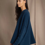 a woman wearing an oversized cashmere sweater in teal blue over silk trousers in bronze