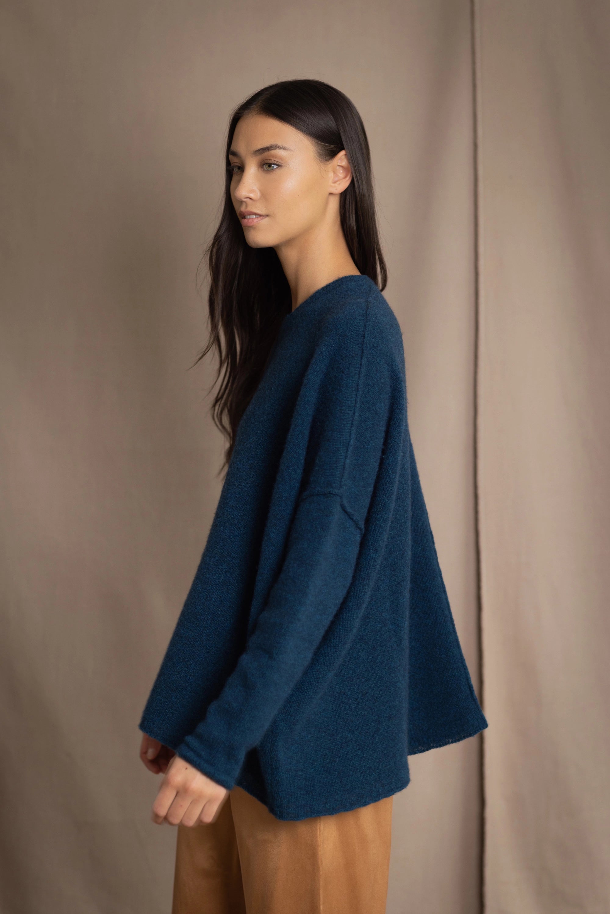 a woman wearing an oversized cashmere sweater in teal blue over silk trousers in bronze