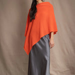 a woman wears a cashmere cape in orange with matching cashmere beanie hat over grey silk skirt